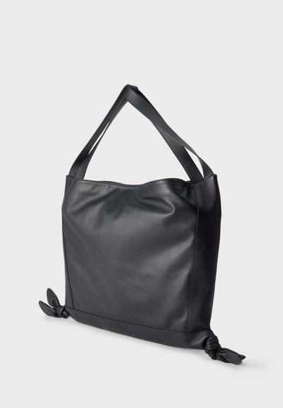 Sac fourre-tout en cuir noir avec deux bretelles et des détails noués aux deux coins inférieurs sur un fond uni.