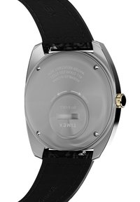 Fond de montre en acier inoxydable argenté avec un texte gravé. Bracelets en cuir noir avec finition texturée, présentant une couronne et des éléments en finition dorée.