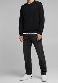 Sudadera negra de cuello redondo sobre una camiseta blanca, combinada con jeans oscuros y zapatillas blancas con detalles negros. Tela suave y ajuste casual.