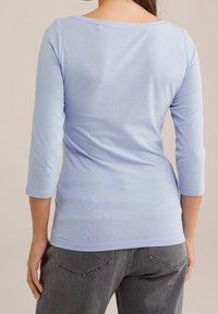 Ljust blå, åtsittande långärmad topp med vid halsringning och trekvartsärmar, gjord av mjukt tyg. Bärs med mörkgrå jeans.