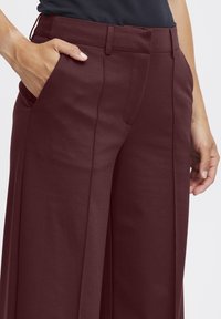 Burgunderrote weite Hosen aus glattem Material, mit flachem Bund und Seitentaschen. Kontrollierte Passform an der Taille.