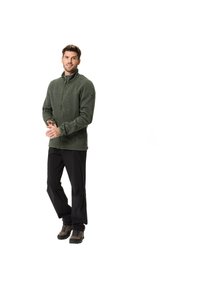 Grüne Fleecejacke mit hohem Kragen, Frontreißverschluss und strukturiertem Stoff. Kombiniert mit schwarzen Hosen und braunen Wanderschuhen.