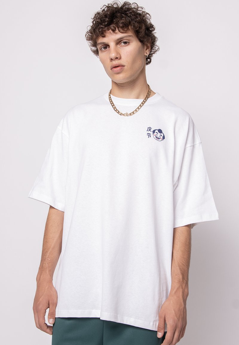 White oversized cotton t-shirt featuring a blue graphic design and text on the left chest. Short sleeves and a crew neckline.