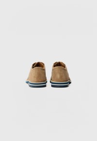 Braune Wildlederschuhe mit abgerundeten Fersen, hellblau-weiß gestreifter Sohle und lässigem Design. Die Textur wirkt weich und glatt.