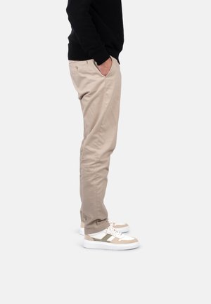 Pantalones beiges de corte relajado con bolsillos laterales, combinados con zapatillas blancas con detalles grises. Se llevan con un suéter negro.