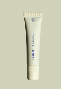 Le Korres True Lip Shine dans un tube vert pâle avec un capuchon à vis, présente un texte bleu indiquant le SPF et les détails du produit. Design lisse et minimaliste.