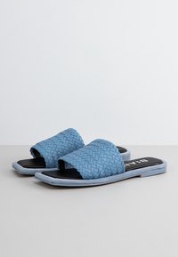 Niebieskie wsuwane sandały z czarnymi podeszwami, o płaskim kroju i teksturowanym wierzchu. Paski są plecione, co dodaje im szczegółów.