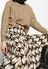 Beiger, strukturierter Strickpullover kombiniert mit einem langen, gemusterten Rock mit braunen, weißen und schwarzen Formen. Lässiger Stil, lockere Passform.