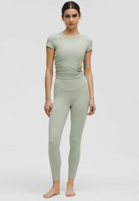 T-shirt a righe verde chiaro con maniche corte e design aderente, abbinato a leggings a vita alta coordinati, entrambi realizzati in materiale elasticizzato.