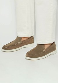 Brown suede slip-on shoes with white rubber soles and decorative stitching along the edges, featuring a smooth texture and simple design.