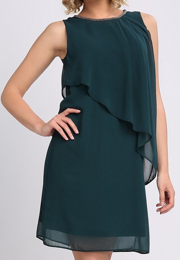 Robe en chiffon superposé vert foncé sans manches avec un col orné de perles, portée par une femme avec une main sur la hanche.