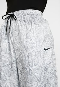 Lätta, grå shorts med ormskinnsmönster, elastisk midja, svart dragsnöre och en diskret svart Nike-logotyp på sidan.