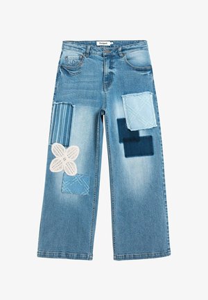 Lyseblå denimjeans med flere dekorative patches, herunder stribet stof, mørkeblå firkanter og en hvid blomstret blondepatch.