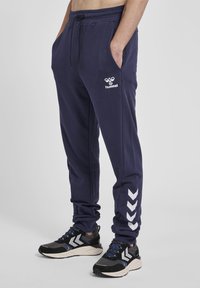 Marineblaue Jogginghosen aus weichem Stoff, mit elastischem Bund, seitlichen Taschen und weißem Markenlogo mit Akzentstreifen an den Seiten.