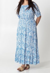 Blå blommig maxi-klänning med korta ärmar, elastisk midja och volangkant. Tillverkad av lätt tyg med ett vitt mönster av blad och blommor.