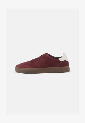 Tenis de camurça cor bordeaux com costura tonal, um suporte de calcanhar branco em contraste e uma sola de borracha castanha. Design simples e de perfil baixo.