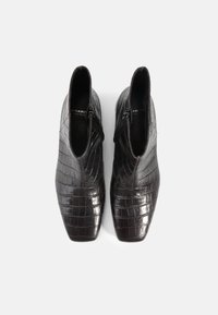 Bottines en cuir noir avec une texture crocodile, design à bout pointu et zips latéraux pour la fermeture, mettant en valeur une silhouette moderne et épurée.
