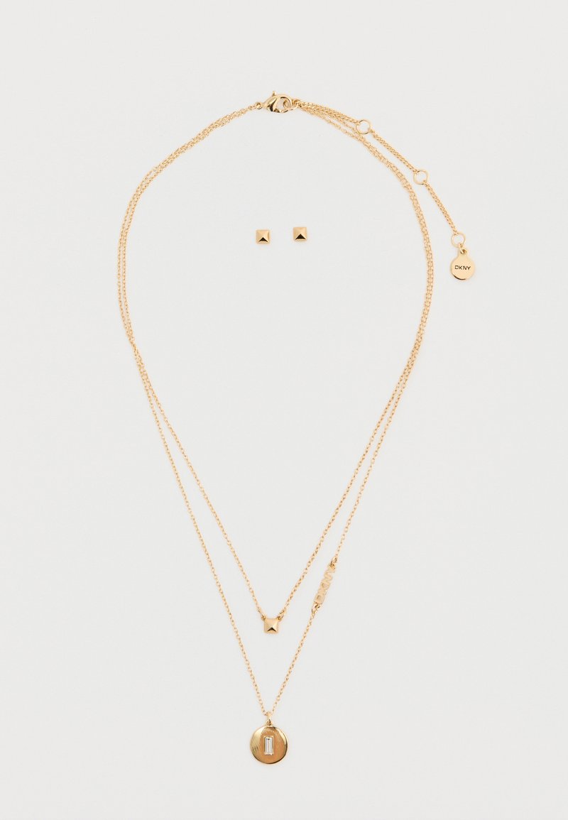 Collana a più strati in tonalità oro, con pendente circolare testurizzato, accento a stella e lettere in blocco; abbinata a orecchini a forma geometrica.