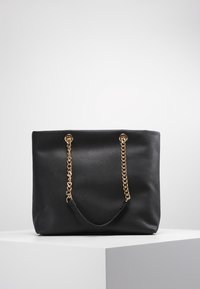 Svart syntetisk tote-väska med en slät yta, utrustad med guldkedjor som handtag och en rymlig design. Inga synliga logotyper eller mönster.