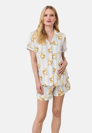 Kvinde iført matchende kortærmet skjorte og shorts med gult andemønster og lyseblå lodrette striber på hvid baggrund.