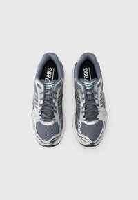 Αθλητικά παπούτσια Asics με γκρι επάνω μέρος από δίχτυ με ασημί λεπτομέρειες, σύστημα κορδονιών, μαλακή σόλα και επενδύσεις με λογότυπο.