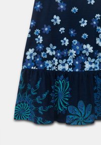 Abito blu navy con motivi floreali bianchi e blu, caratterizzato da un orlo arruffato decorato con intricati ricami floreali in turchese e verde.