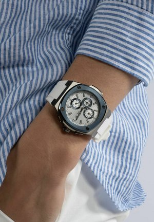 Armbåndsur med et sølvfarvet hus, hvid silikoneurrem og en hvid urskive med tre sub-urskiver. Blå accenter på huset og hardware.