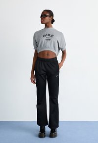 Pelēks apgriezts svīteris ar melnu "NIKE" logotipu, kam pievienotas melnas bikses ar elastīgu jostu, uz kurām ir neliels balts zīns, un melnas platformas zābaki.