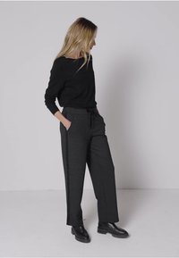 Czarny sweter z dekoltem w łódkę, zestawiony z szarymi, luźnymi spodniami z bocznymi kieszeniami i troczkami w pasie. Czarne botki za kostkę.