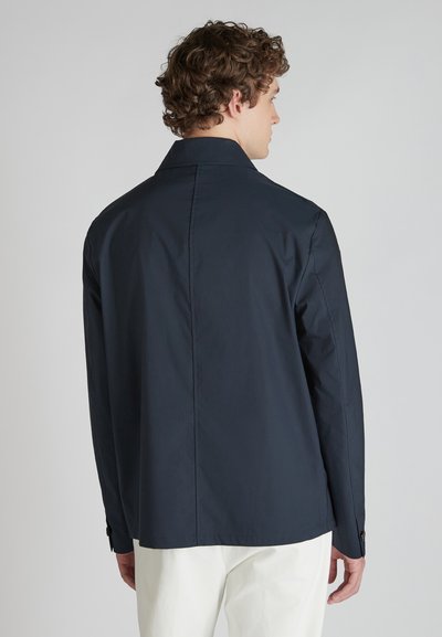 Granatowa kurtka o usztywnionej konstrukcji, z długimi rękawami i kołnierzem. Gładka tekstura z guzikami na mankietach i prostym szwem z tyłu.