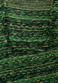 Pletený zelený oděv, který se vyznačuje různými odstíny zelené a černé příze, s texturovaným vzorem a jemnými metalickými nitěmi po celé ploše.