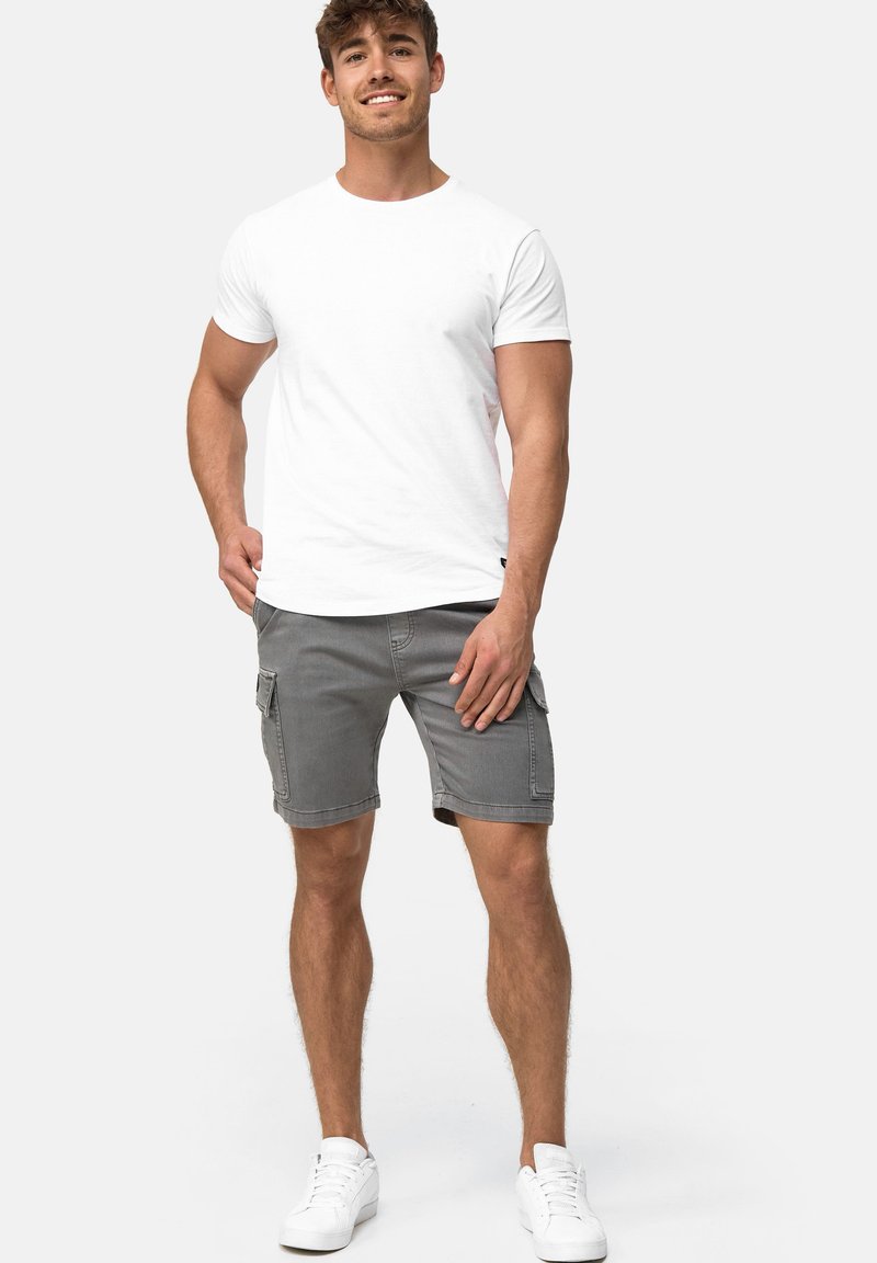 T-shirt en coton blanc associé à un short cargo gris, avec des poches latérales, le tout accompagné de baskets blanches pour un look décontracté.
