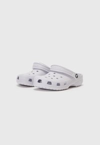 White plastic clogs with ventilation holes, a raised back strap, and textured soles, featuring a circular brand emblem on the side.