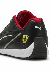 Baskets en cuir noir avec des accents rouges, semelle blanche et logo Puma. Équipées de l'emblème Ferrari et d'un décor texturé sur la tige.