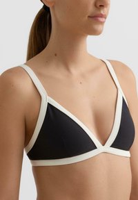 Črni modrček v obliki trikotnika z belim robom, tankimi nastavljivimi naramnicami, gladkim materialom in globokim V izrezom. Minimalistična zasnova brez vidnih kovinskih delov.