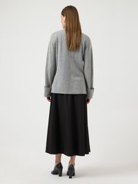 Γυναίκα που φαίνεται από την πλάτη, φορά γκρι πουλόβερ με μακριά μανίκια, μαύρη midi φούστα και μαύρα ψηλοτάκουνα παπούτσια, με ίσια μακριά μαλλιά.