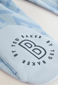 Svetlomodrá látka s geometrickým vzorom, v strede s čiernym kruhovým logom s nápisom "TED BAKER BY TED BAKER". Mäkka textúra.