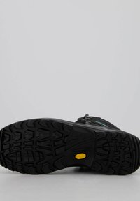 Zwarte wandelschoen met een zool met diepe traction lugs, Vibram-logo, een getextureerd rubberoppervlak en een gebogen ontwerp voor stabiliteit en grip.