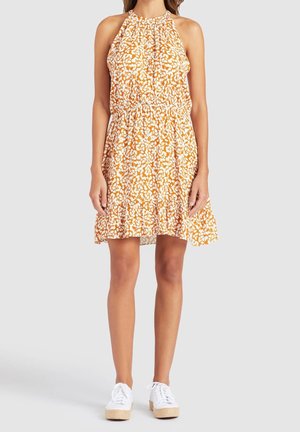 Oranger Neckholder-Kleid mit weißem Blumenmuster, tailliert und mit ausgestelltem Rock. Kombiniert mit weißen Sneakern mit Keilabsatz aus Jute.