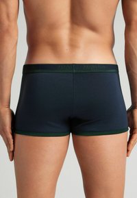 Mörkblå boxerkalsonger med grön midjeband och kant. Slät tygtextur, minimala sömmar och en bekväm passform som är designad för rörelse.