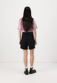Svarte denimshorts med en avslappet passform, kombinert med en lys lilla t-skjorte med dekorativ trim. Langt, rett hår synlig.