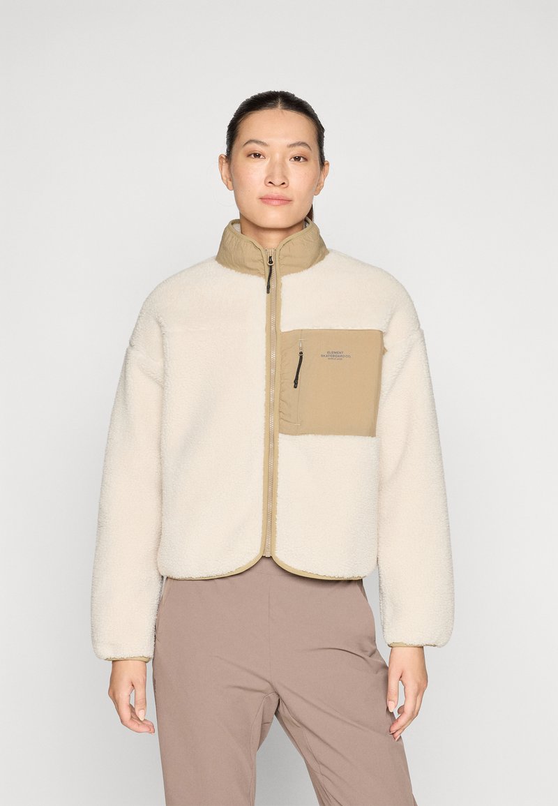Giacca in pile color avorio con una tasca sul petto beige. Presenta un colletto alto e chiusura con zip, con bordi in contrasto e una texture morbida.