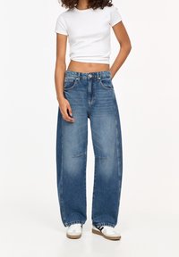 Siniset leveälahkeiset denim-farkut, joissa on korkea vyötärö, etutaskut ja haalistunut pesu. Yhdistetty tiukkaan valkoiseen crop topiin ja lenkkareihin.