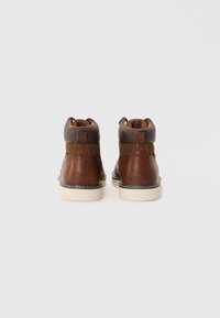 Botas de tobillo de cuero marrón con forro acolchado marrón, suela de goma blanca y costuras en contraste. Acabado suave con puntera redondeada.
