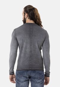 Langärmliges graues T-Shirt mit verblasster, strukturierter Optik; verfügt über einen runden Halsausschnitt und eine Mittelnaht am Rücken. Kombiniert mit blauen Jeans.