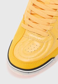 Sárga sneaker sima és texturált bőrből készült, perforált részletekkel és lapos fűzőkkel. Fekete-fehér gumi talp.