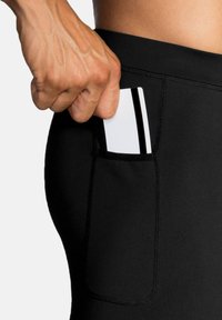 Juodos sportinės legging kelnės su šonine kišene, pasižyminčios glotnia tekstūra ir sustiprinta siūle, kai į kišenę įdedama kortelė.