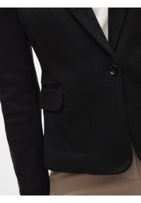 Zwarte blazer met een gestructureerde afwerking, enkele knoopsluiting en een klein linkerzakje. Heeft een getailleerde pasvorm en gladde revers.