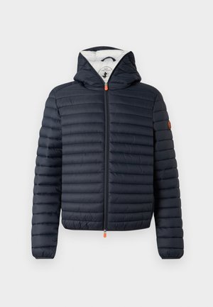 Giacca imbottita blu navy con zip frontale, cappuccio e design trapuntato orizzontale. Presenta una cerniera arancione e un logo sulla manica sinistra.