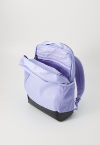 Sac à dos en tissu violet à texture en maille, avec un fond noir, une poche extérieure zippée et des bretelles ajustables, partiellement dézippé.